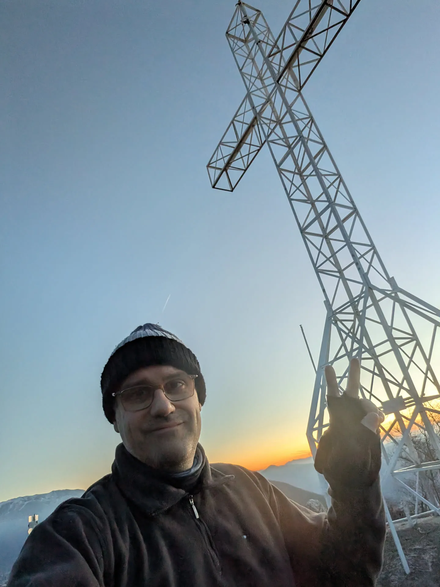 Sergio in vetta, sotto una grande croce di metallo, al tramonto.